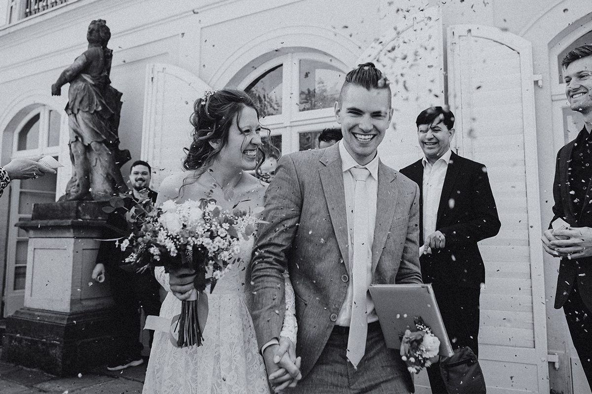 Ein Schwarz-Weiß-Foto einer Braut und eines Bräutigams, die mit Konfetti beworfen werden.